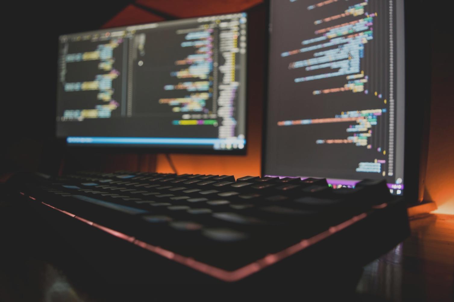 Students working on game development projects with multiple monitors showing code editors and game interfaces